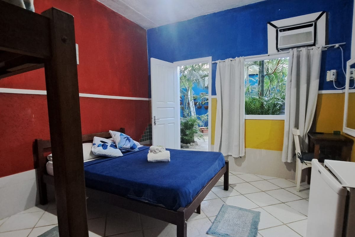 A room with a bed, a ceiling fan, a window with curtains, and a view of greenery outside.