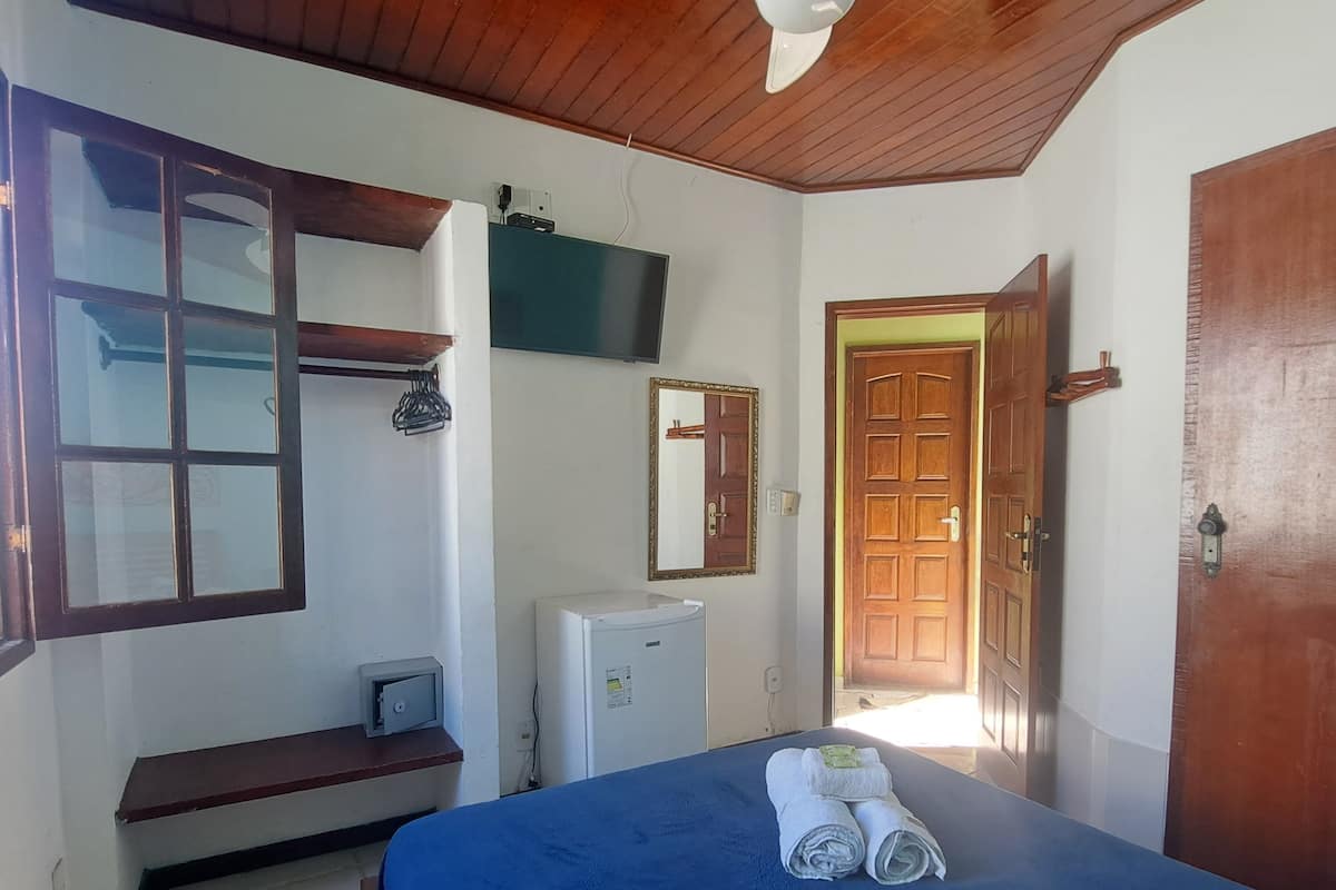 A room with a bed, a ceiling fan, a television, a small refrigerator, and a wooden door.