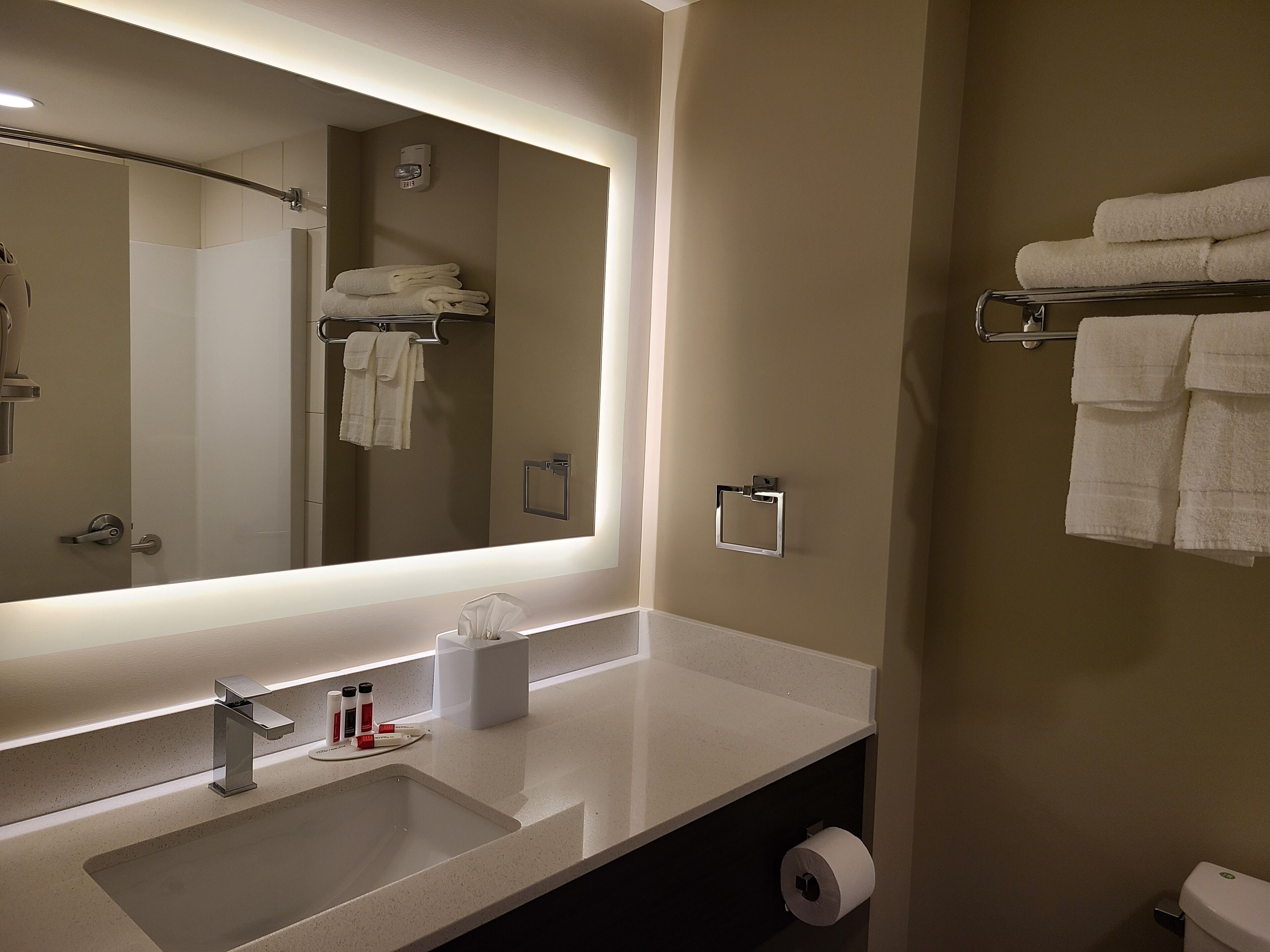 A modern bathroom with a large mirror, a sink, and a towel rack.