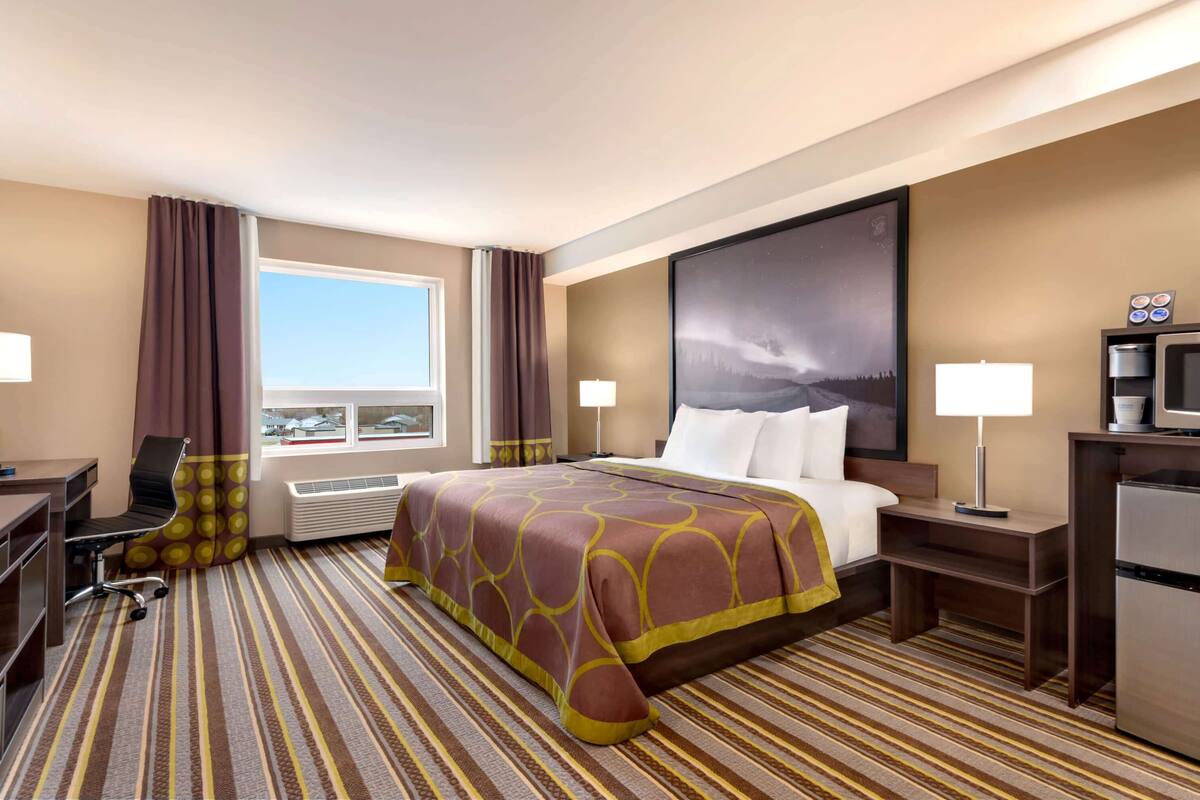 A hotel room with a large bed, a desk, a chair, a TV, and a window with curtains.