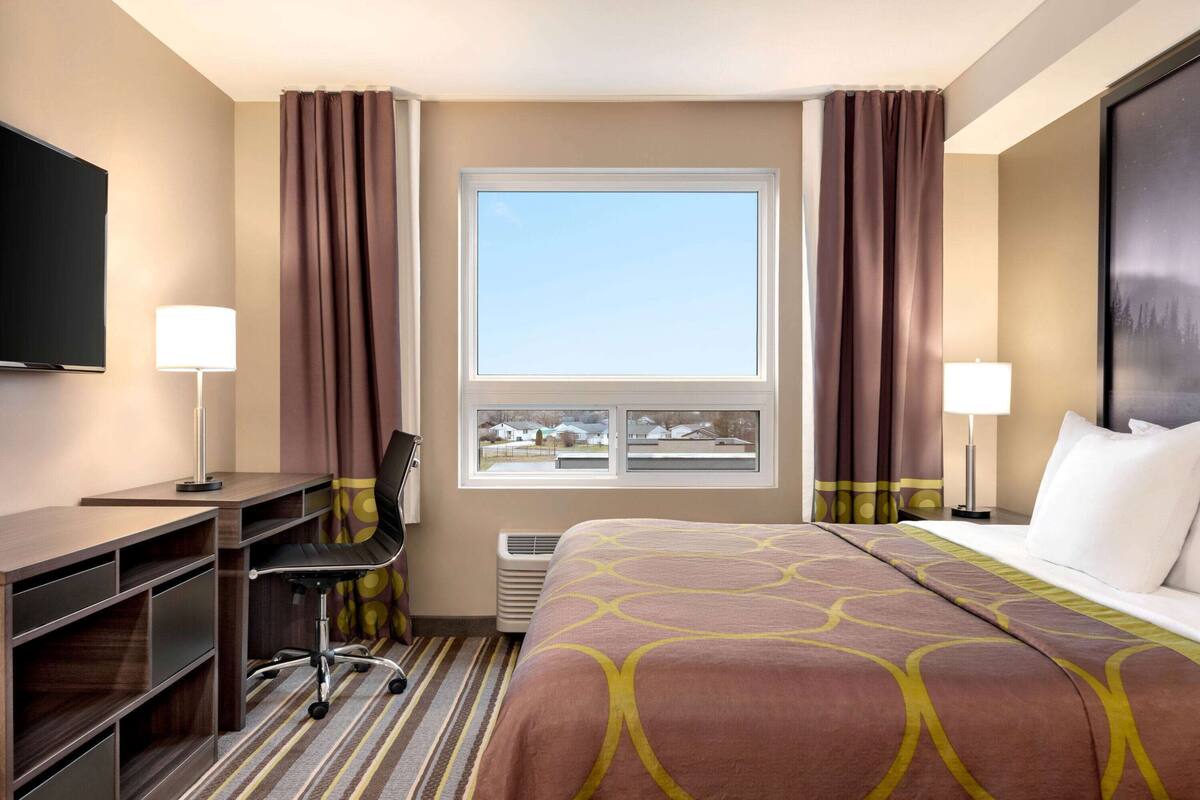 A hotel room with a large bed, a desk with a chair, a TV, and a window with curtains.