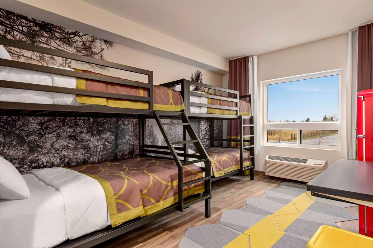 A room with bunk beds, a window with a view, a red table, and a radiator.