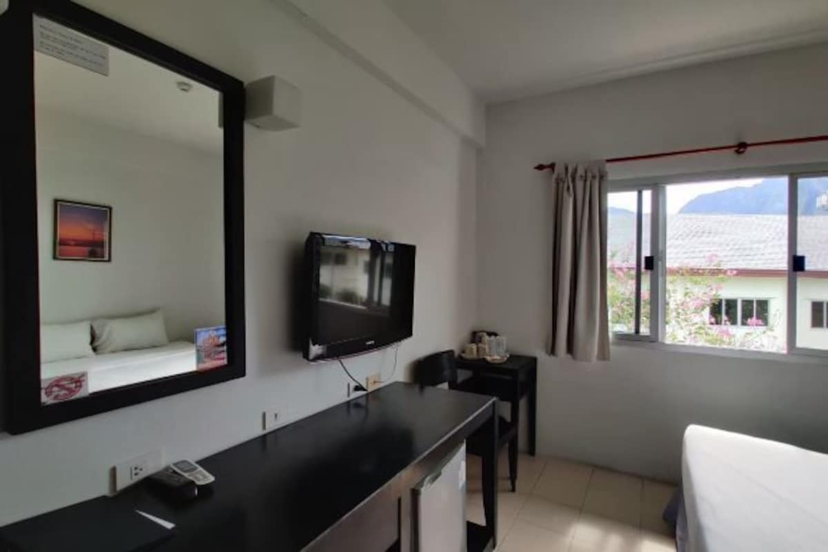 A hotel room with a bed, a TV, a desk, a chair, a window with curtains, and a view of the outside.