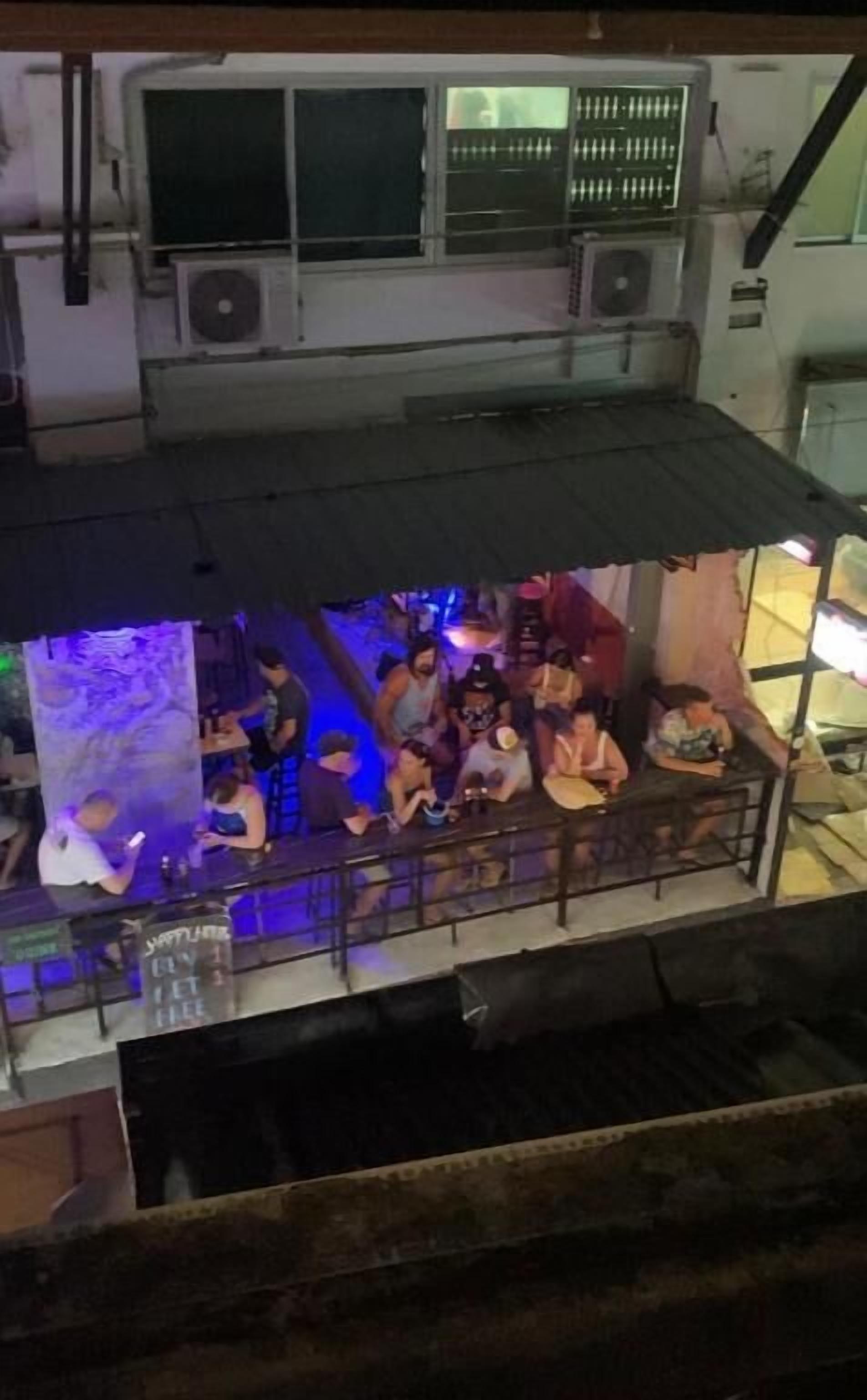 Un bar situé sur le toit d’un immeuble, offrant une vue sur la ville, avec des places assises en plein air et un grand mur illuminé.