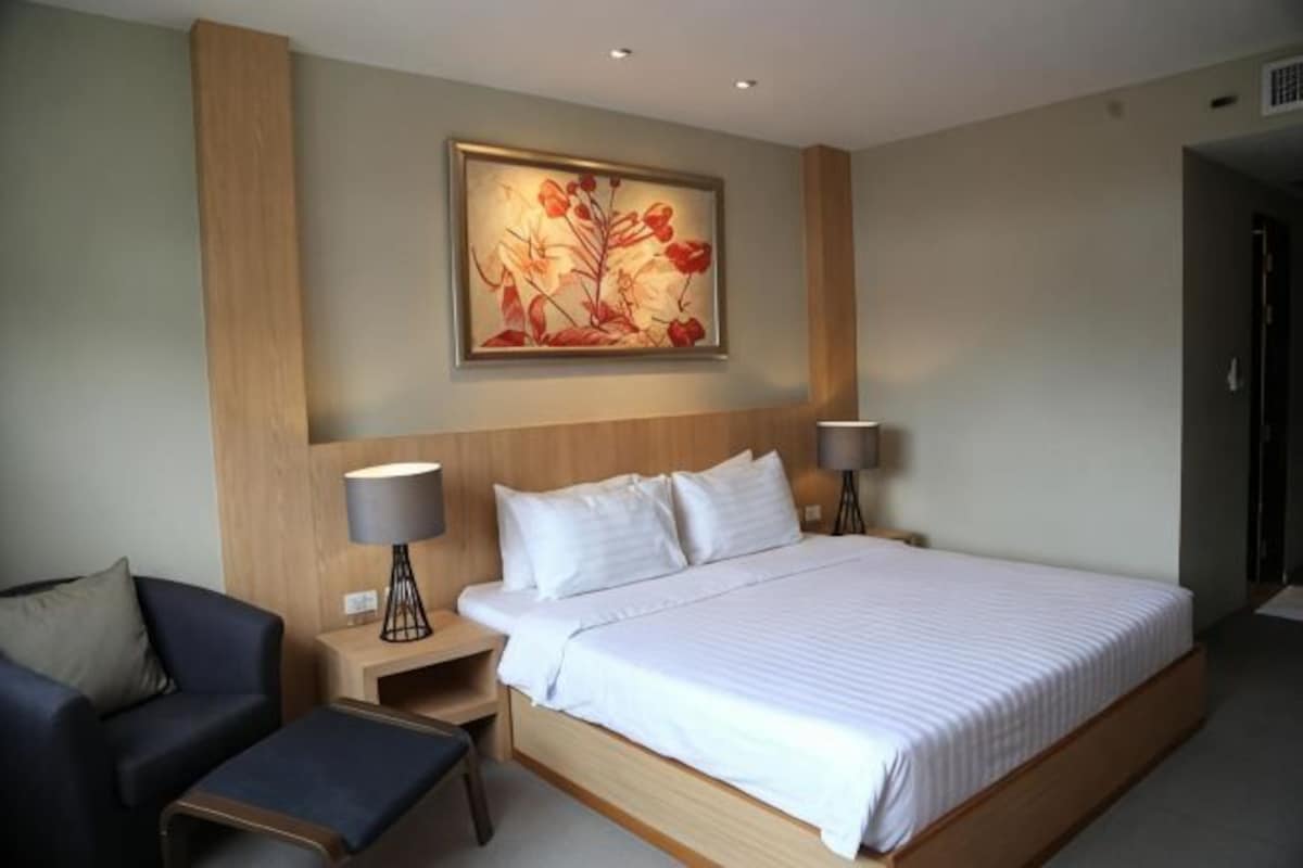 A hotel room with a large bed, two bedside lamps, a chair, a desk, and a painting on the wall.