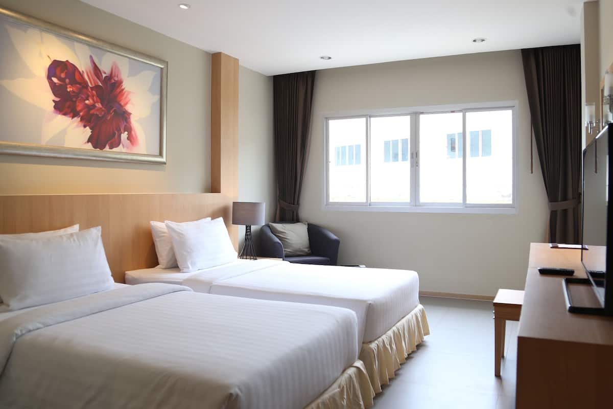 A hotel room with two beds, a desk, a chair, a large window, and a painting on the wall.