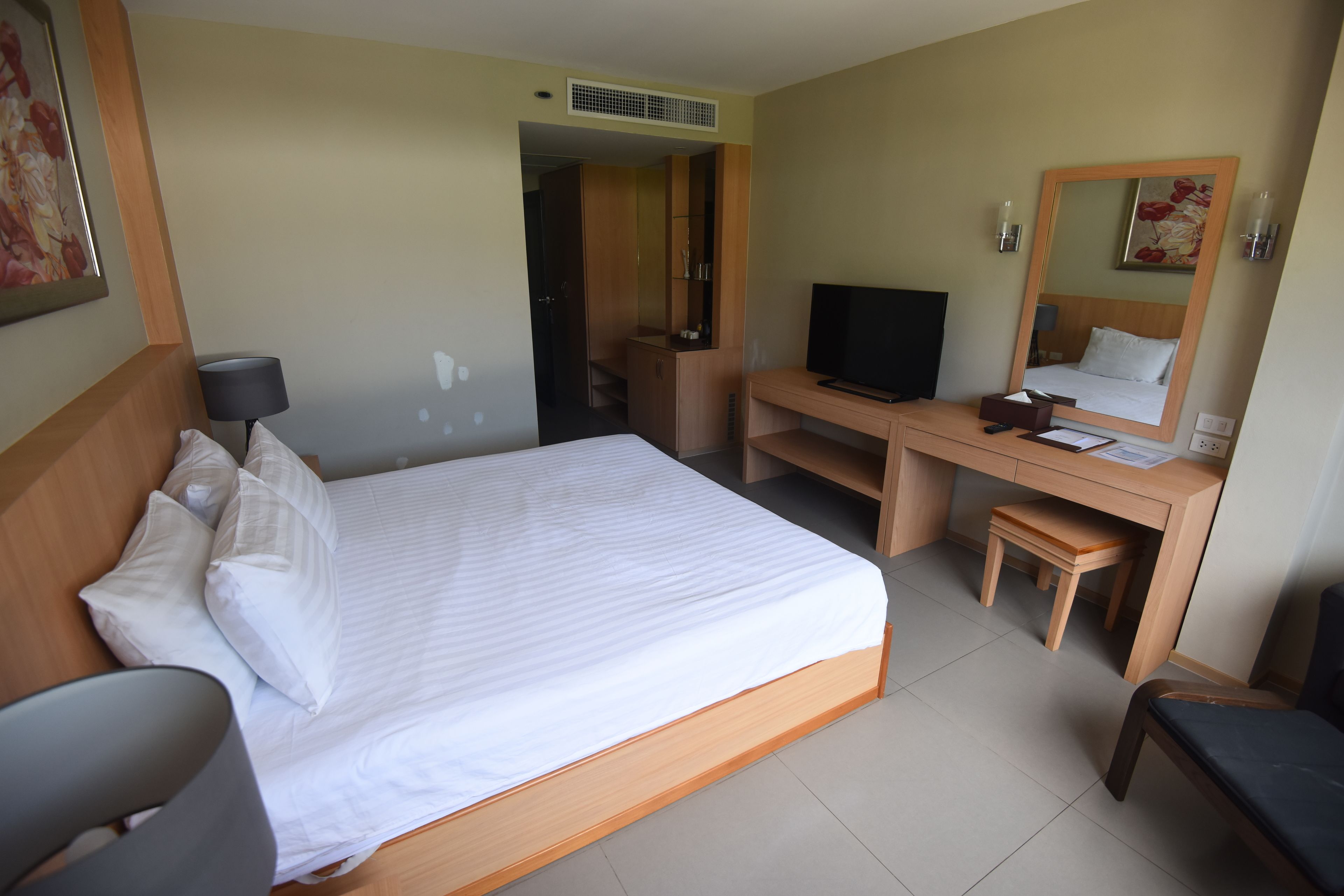 A hotel room with a bed, desk, TV, and a mirror.