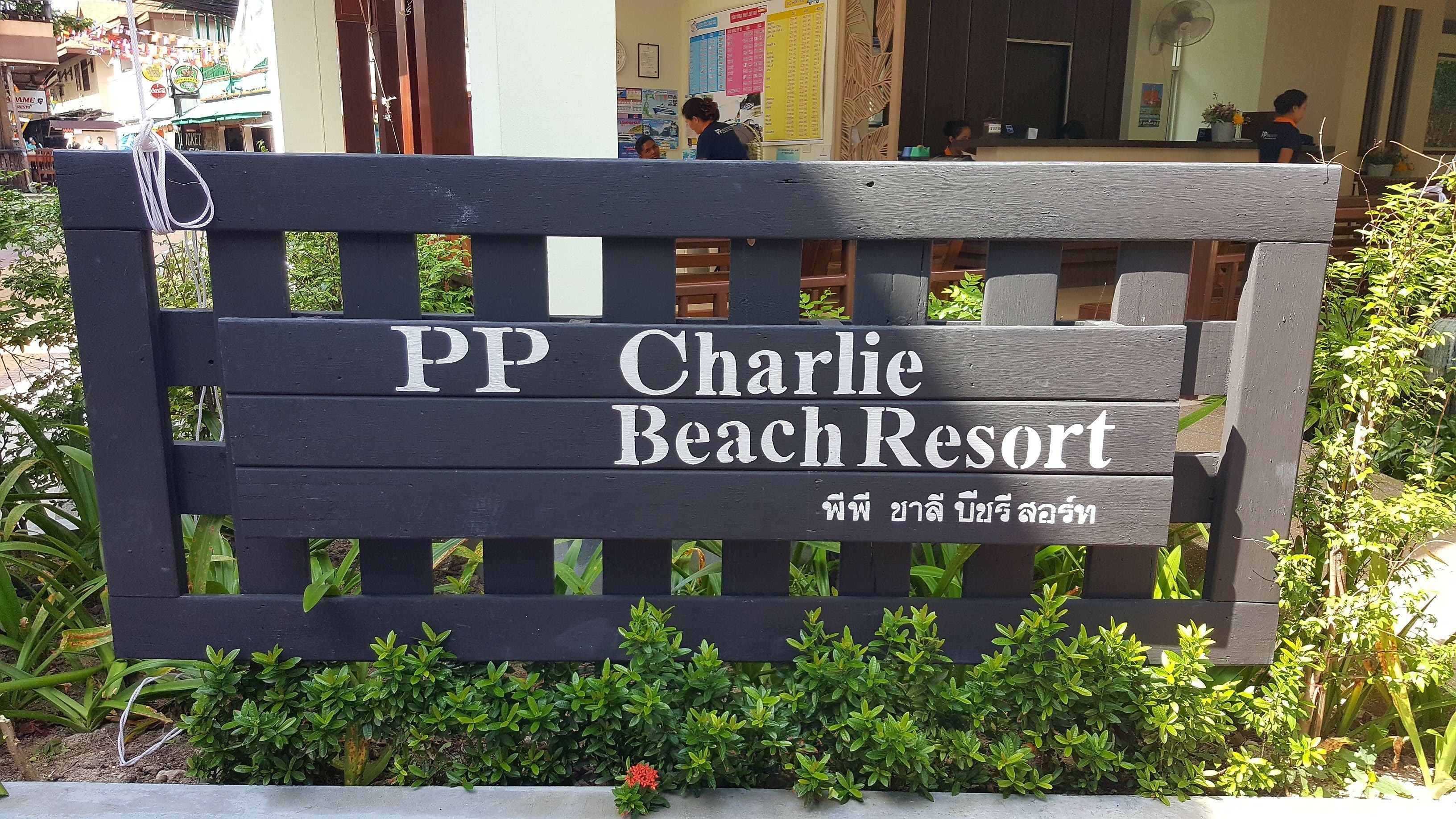 A wooden sign with 'PP Charlie Beach Resort' written on it, surrounded by greenery.