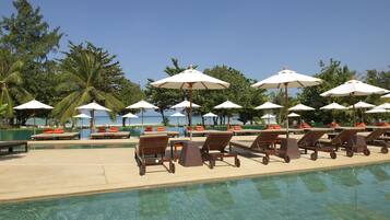 A poolside area with lounge chairs and umbrellas, surrounded by palm trees and a clear view of the ocean.