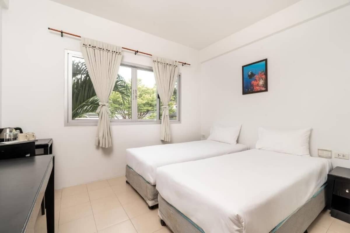 A room with two beds, a desk, a window with curtains, and a painting on the wall.