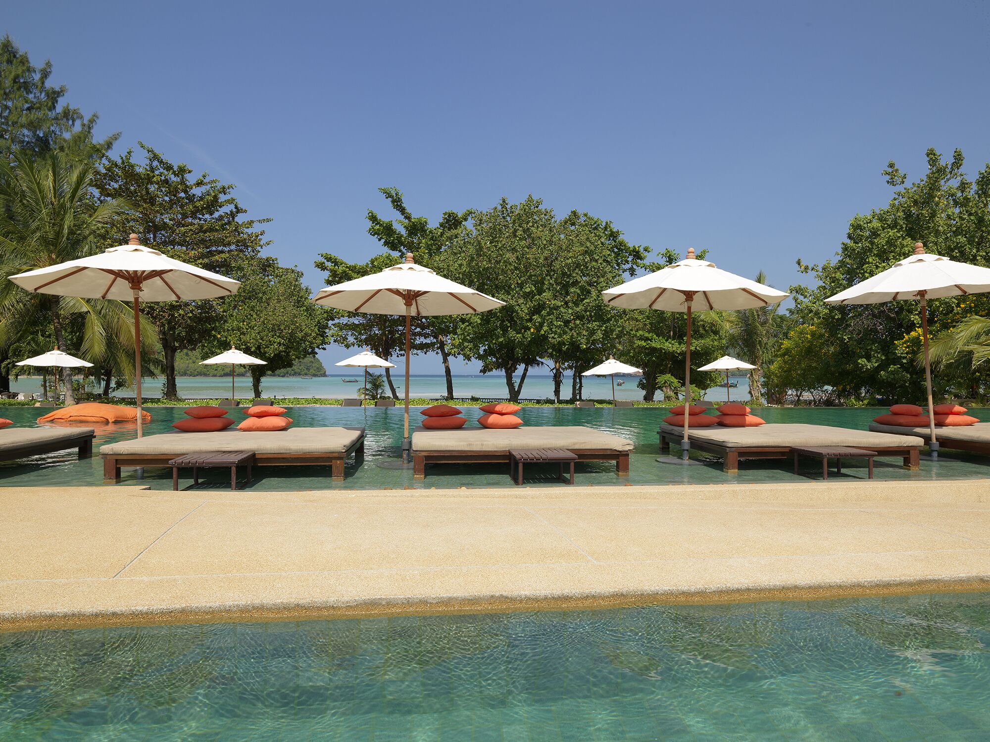 A poolside area with lounge chairs and umbrellas, clear water, and a view of the ocean.