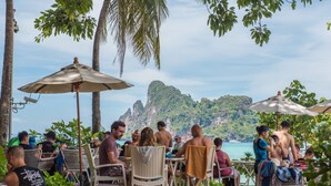 An outdoor seating area with tables and chairs, overlooking a body of water and a mountainous landscape. - PP Charlie Beach Resort (Ko Phi Phi)