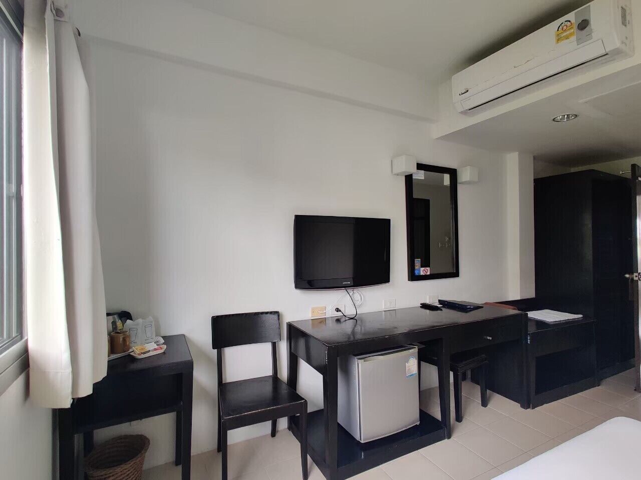 A room with a desk, chair, television, and air conditioning unit.