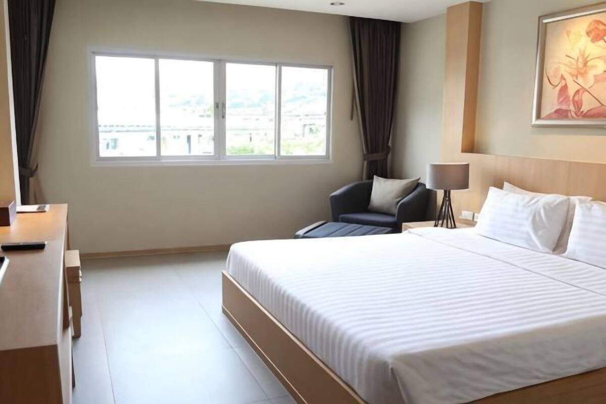 A hotel room with a large bed, a desk, a chair, a lamp, and a window with curtains.