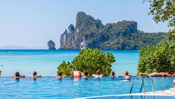 A swimming pool with clear blue water, surrounded by lush greenery and a rocky cliff in the background. - PP Charlie Beach Resort (Ko Phi Phi)