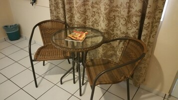 A small room with a round glass table and two wicker chairs. A magazine is on the table.