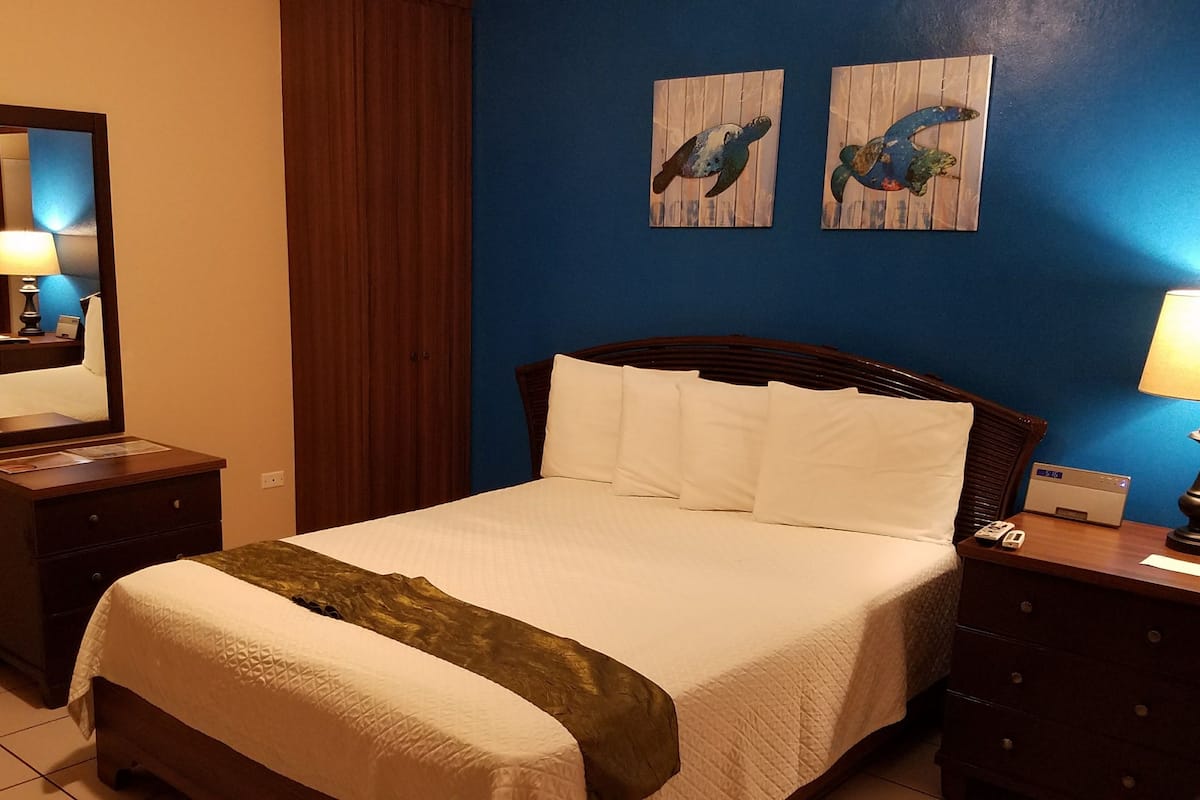 A hotel room with a bed, a nightstand, a dresser, a mirror, and two wall art pieces.