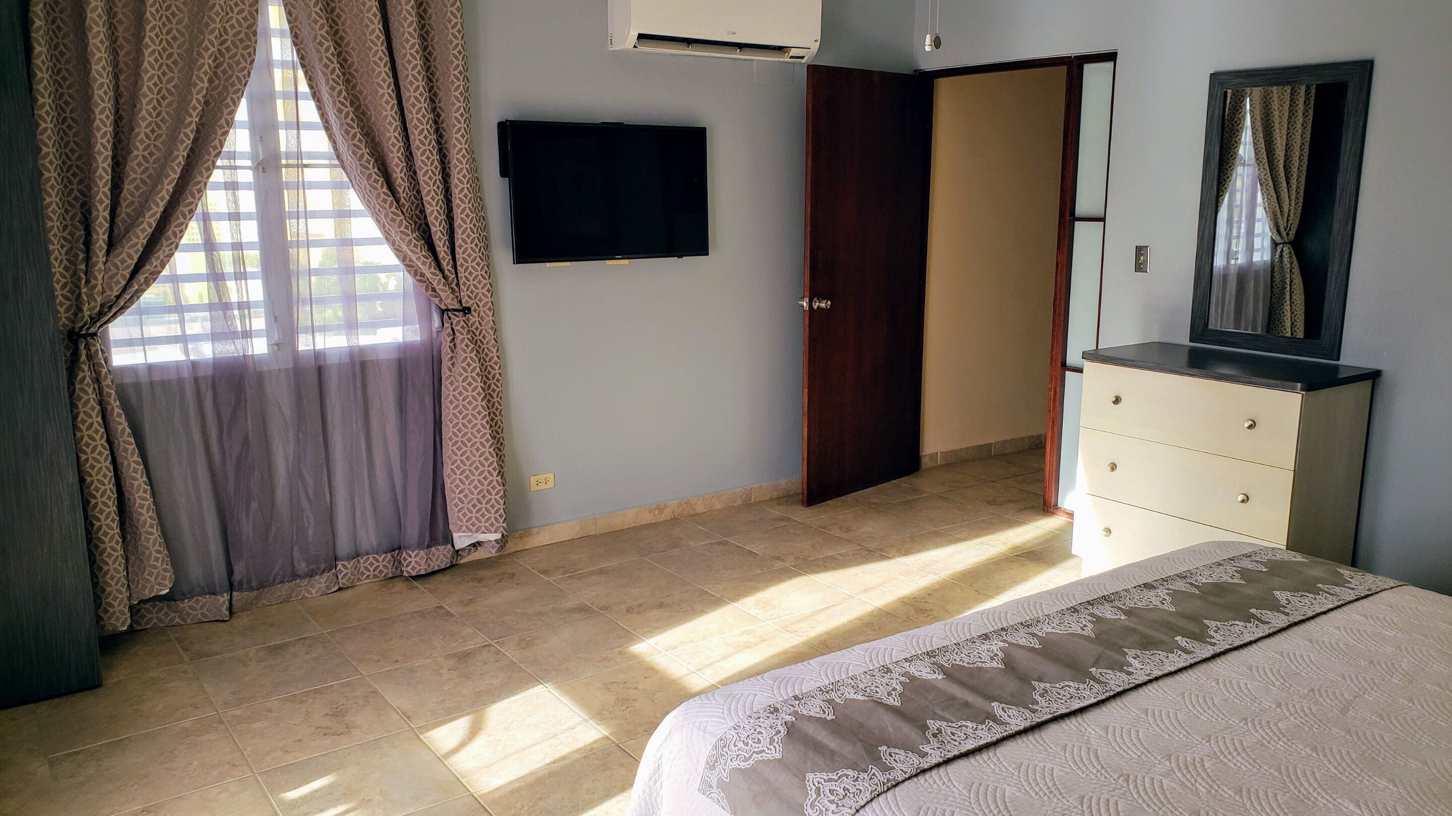 A bedroom with a bed, a dresser, a television, and a door leading to another room.