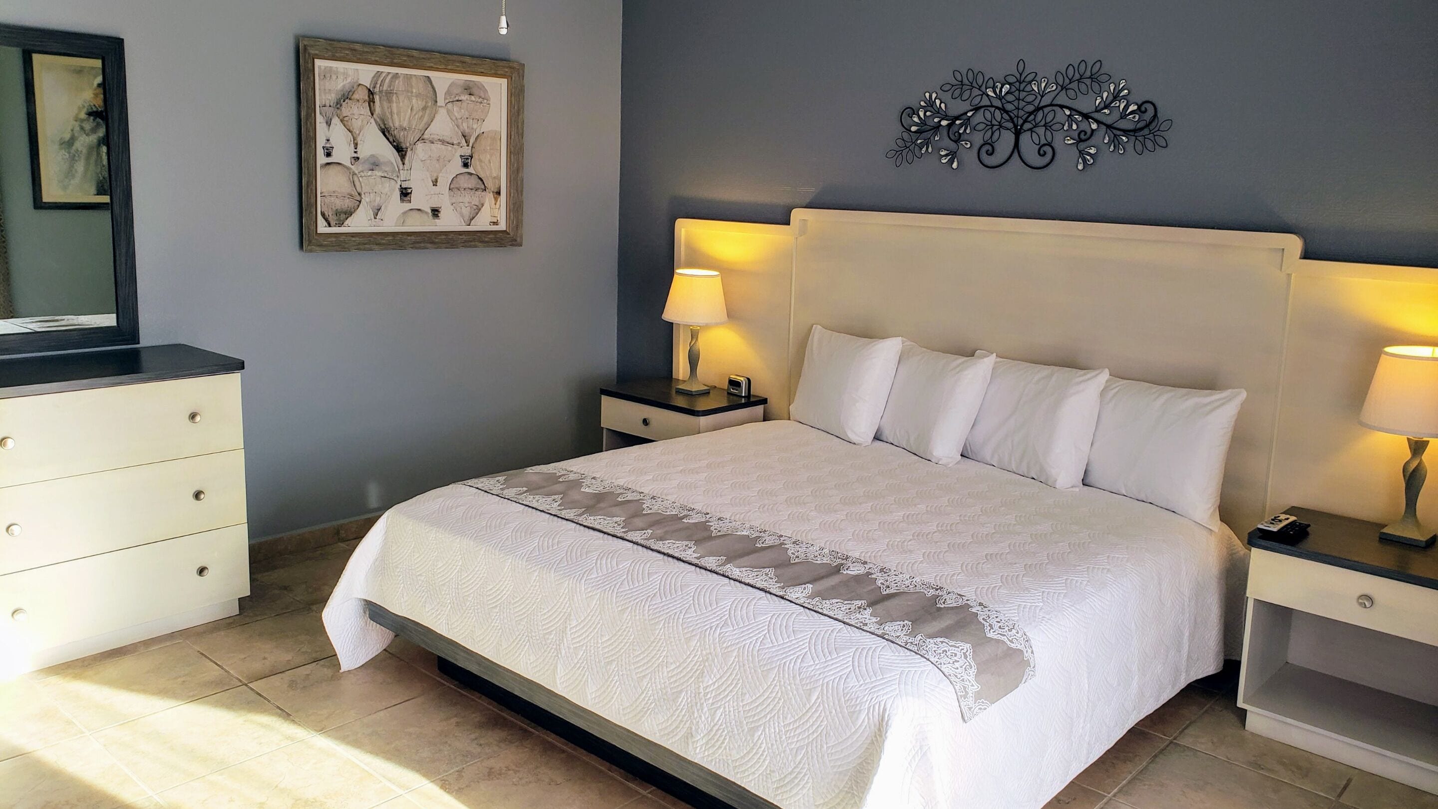 Un dormitorio ordenado con una cama grande, dos mesitas de noche con lámparas, un aparador y una obra de arte enmarcada en la pared.