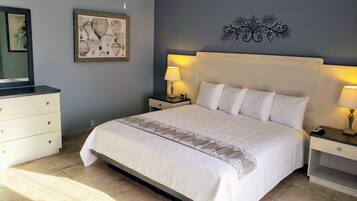 Un dormitorio ordenado con una cama grande, dos mesitas de noche con lámparas, un aparador y una obra de arte enmarcada en la pared.