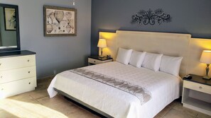 Quarto bem arrumado com uma cama grande, duas mesas de cabeceira com abajures, um aparador e uma obra de arte emoldurada na parede.