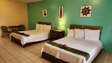 Two double beds with wooden headboards, a small table with chairs, a nightstand with a lamp, and wall art.