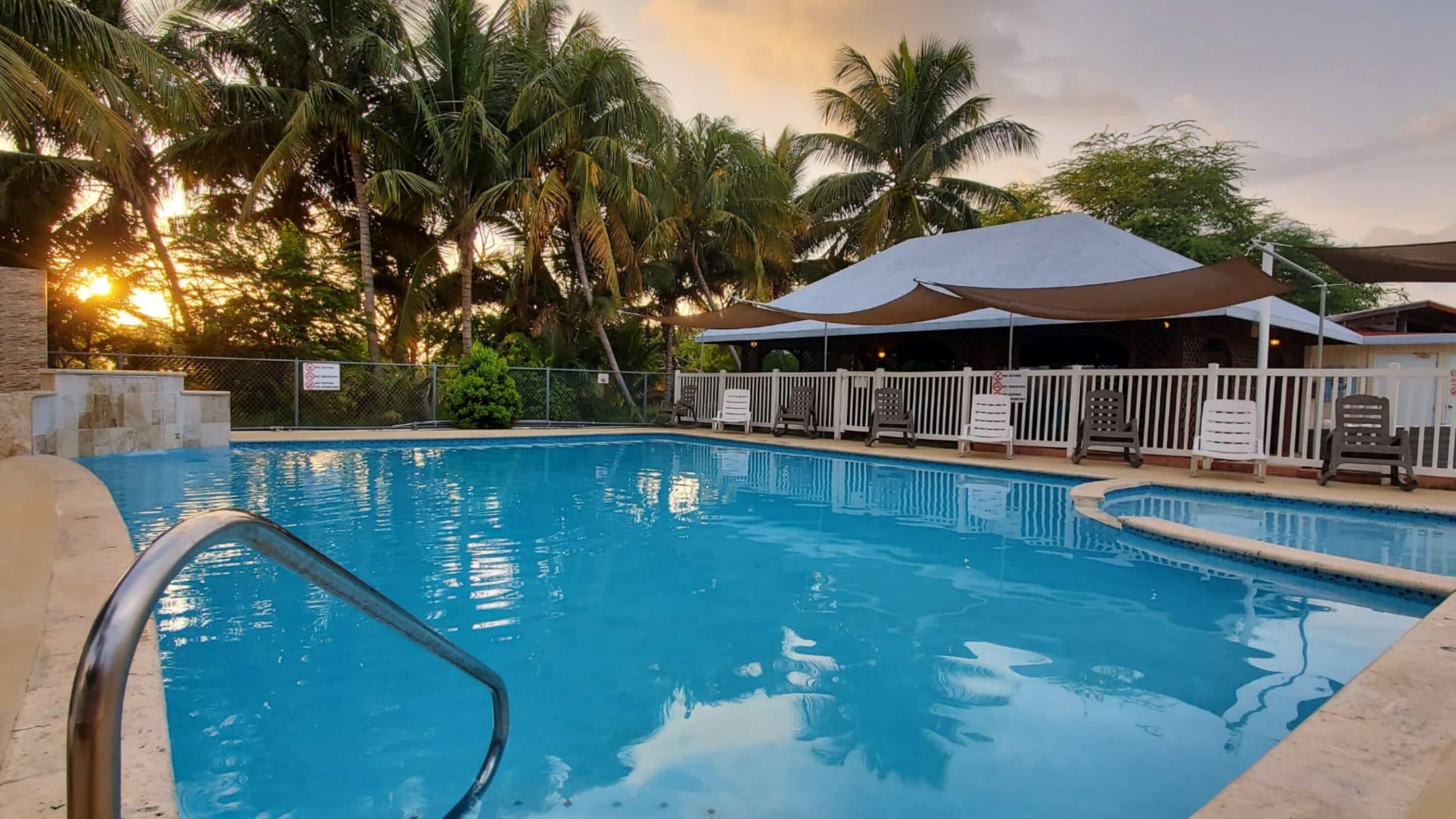 Una piscina con vistas despejadas del entorno, incluyendo una zona de estar cubierta con sillas y una valla.