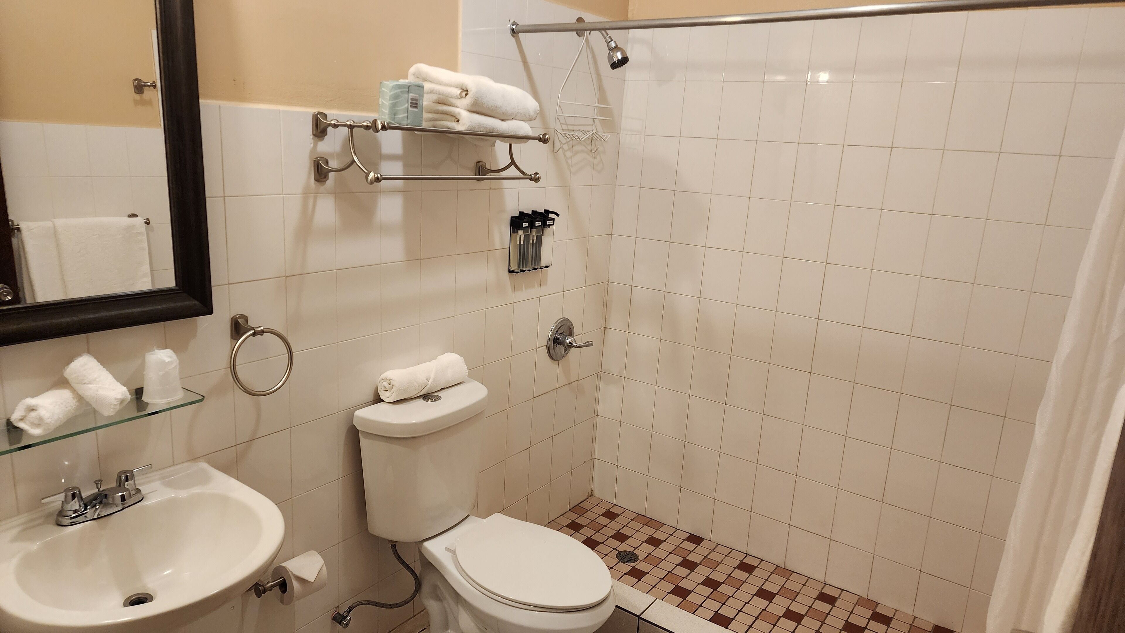 Casa de banho com sanita, lavatório e chuveiro. Há toalhas e artigos de higiene em prateleiras.