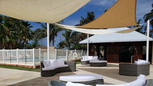 A covered outdoor seating area with wicker furniture and a pool in the background.