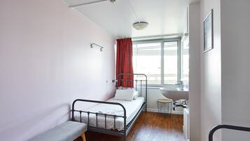 Une petite chambre avec un lit simple, une fenêtre, une table de chevet et un lavabo intégré.
