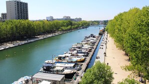 Une promenade au bord de la rivière, avec des bateaux amarrés le long des quais, un chemin piétonnier et des arbres bordant la rivière.
