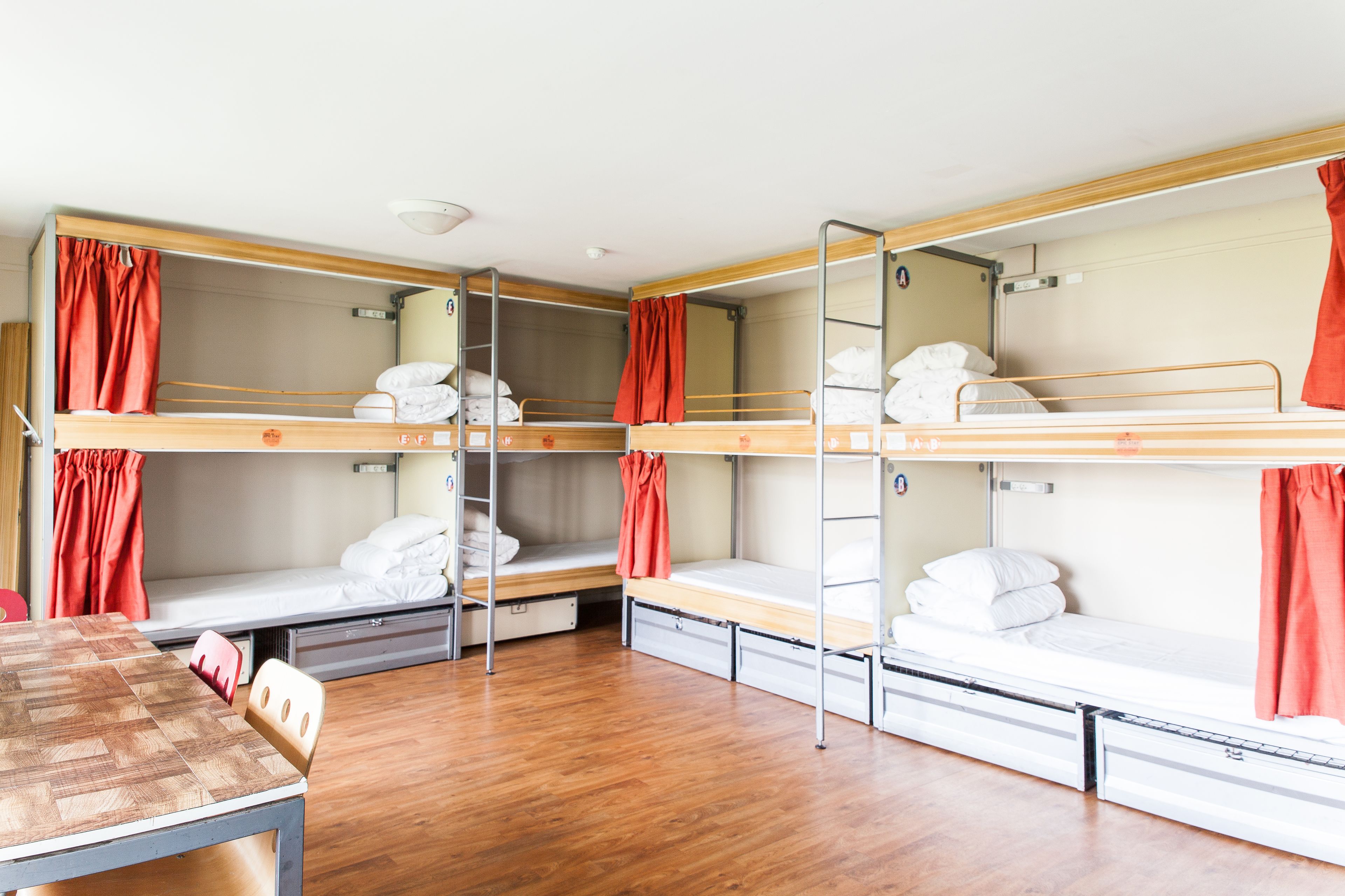 Un dormitorio con literas, una mesa de madera y cortinas rojas.