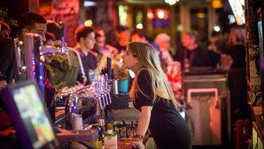Un bar avec un barman préparant des boissons, une caisse enregistreuse, ainsi que diverses bouteilles et verres.