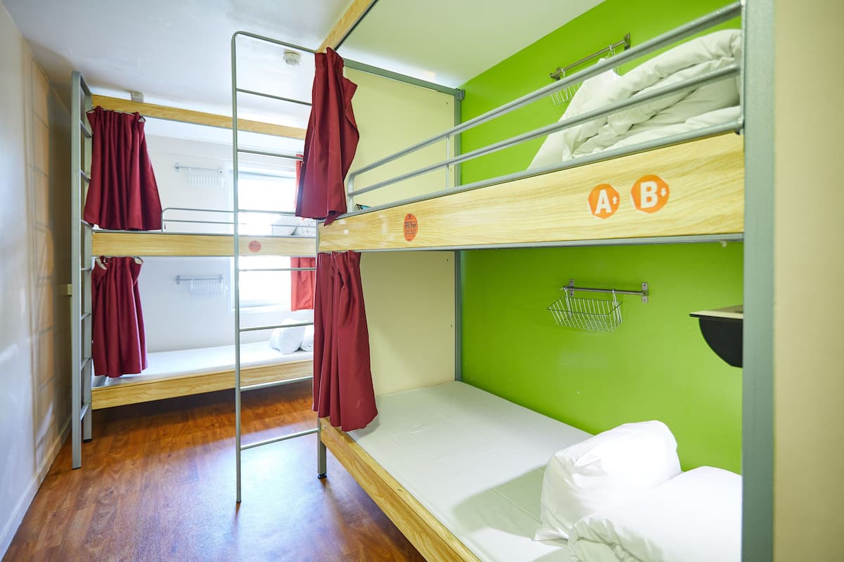 Un dormitorio con literas, suelo de madera y pared verde.