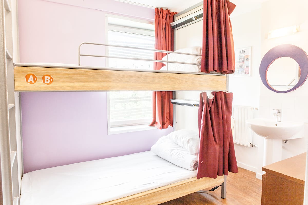 Una cama litera con ventana, un lavamanos y un espejo en una habitación con paredes moradas claras.