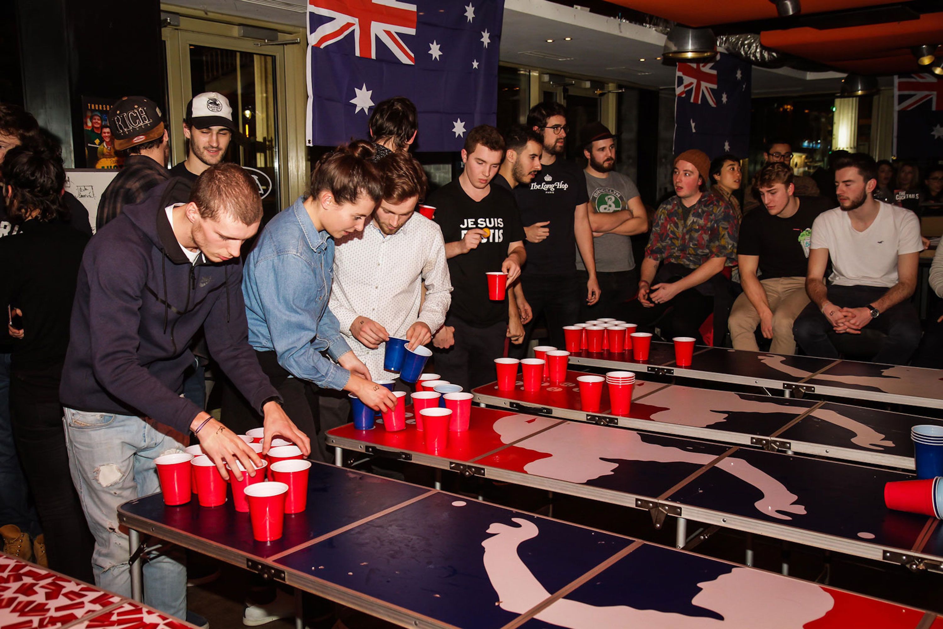 Een groep mensen speelt bierpong aan een tafel, met een Union Jack vlag op de achtergrond.