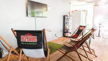 A room with two folding chairs, a television mounted on the wall, and a magazine rack.