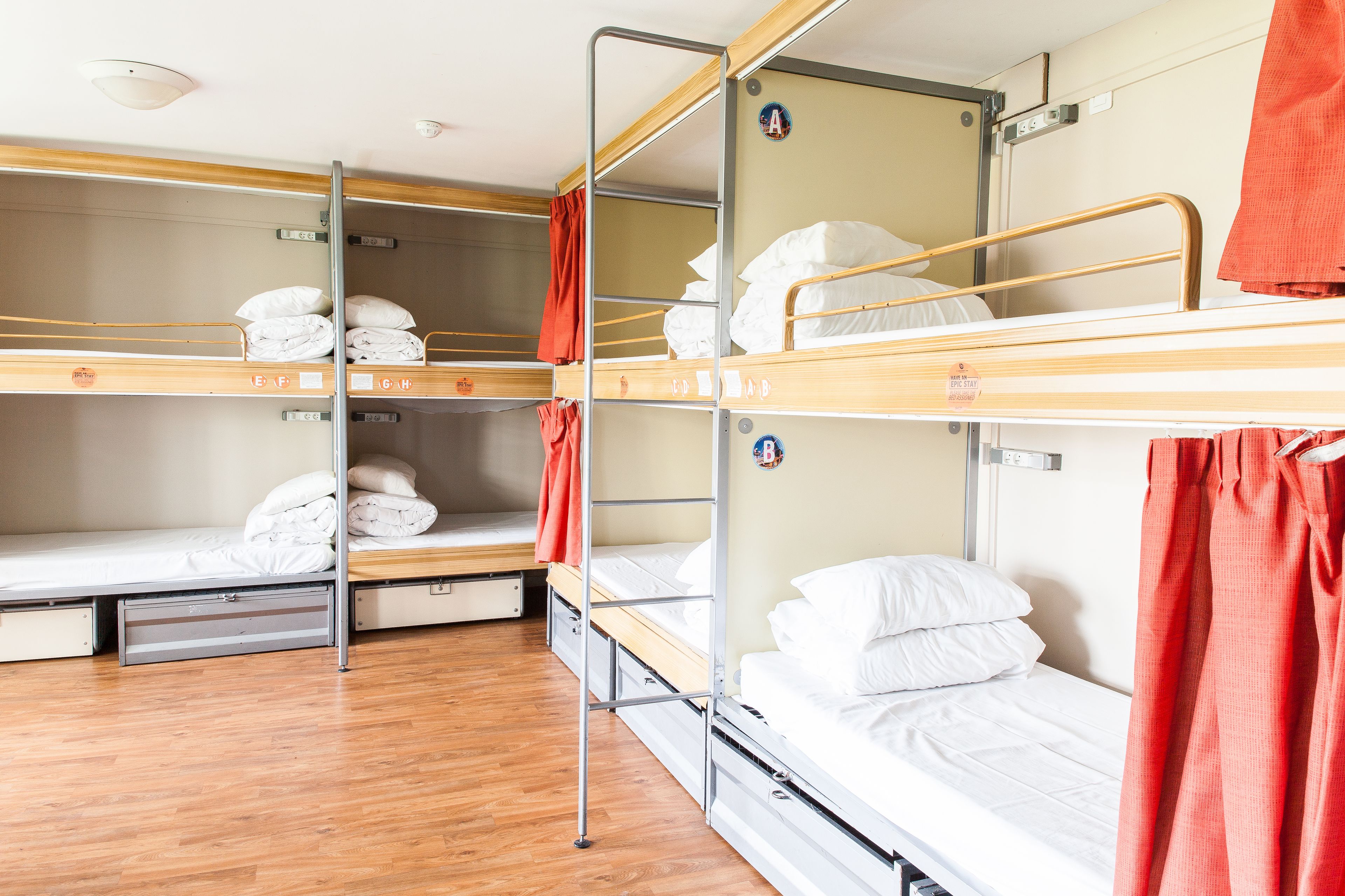 Habitación con literas, piso de madera, barandas de metal y ropa de cama blanca.
