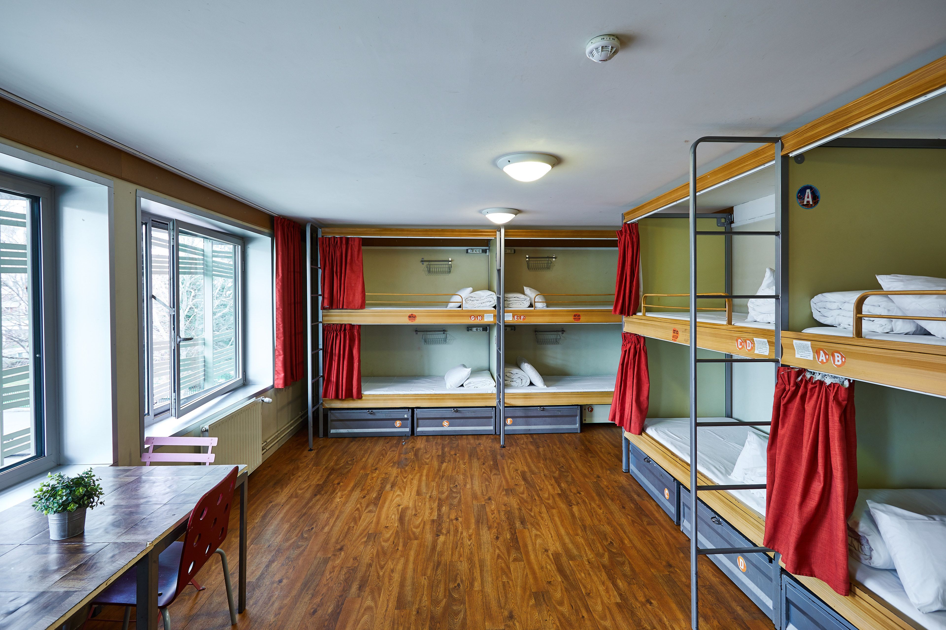 A dormitory room with bunk beds, a wooden table, and a window.