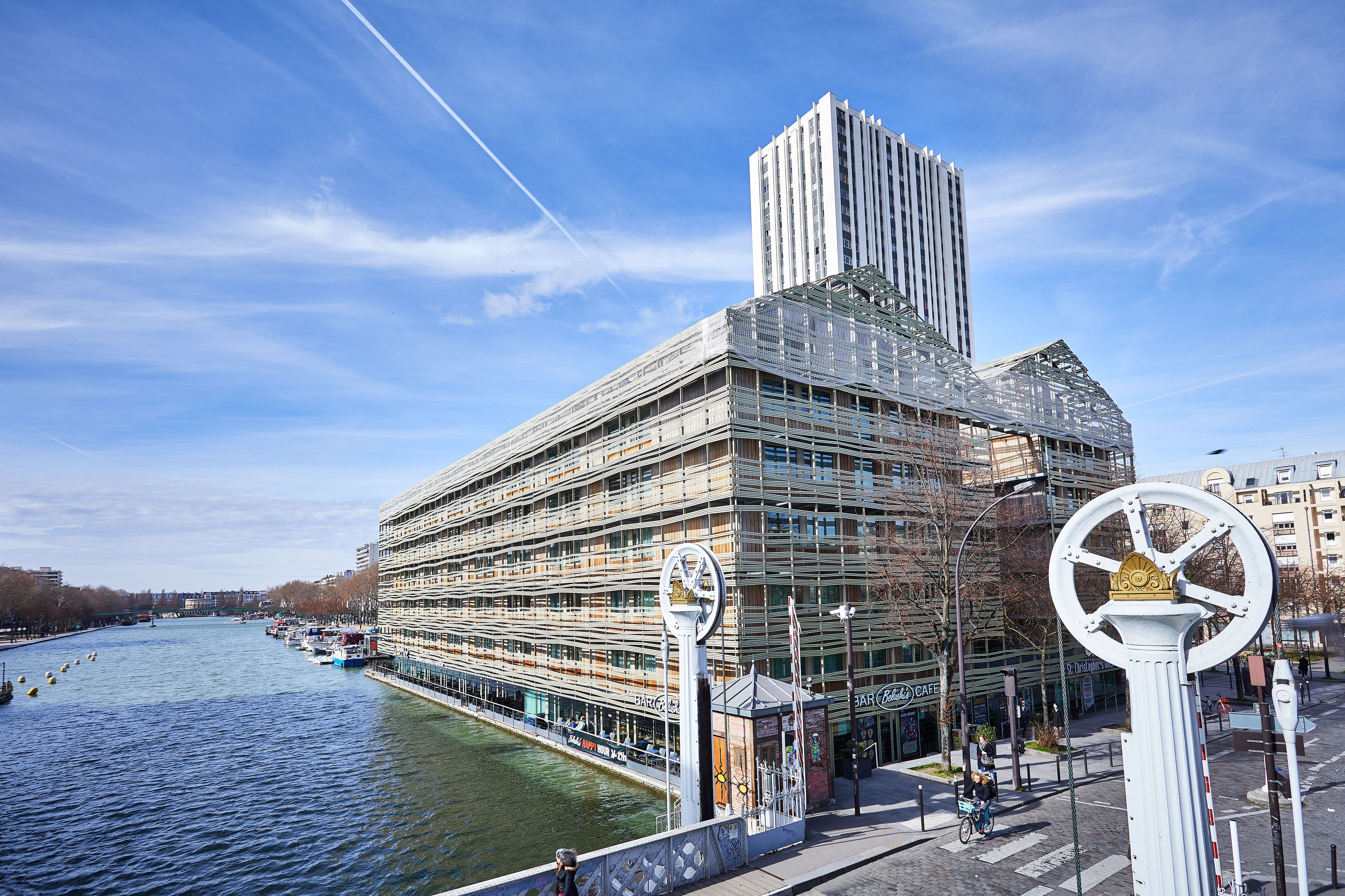 Un edificio moderno con un diseño arquitectónico único, un río en primer plano y un paseo peatonal.