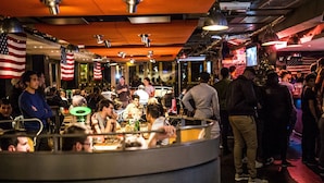 Un bar bondé, décoré de drapeaux américains, où les gens sont debout et assis à des tables, avec un comptoir.