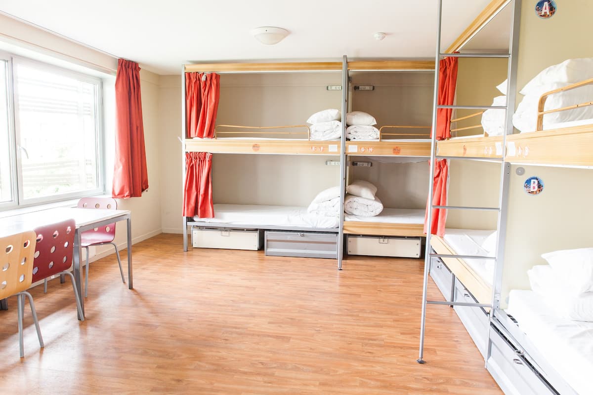 Un dormitorio con literas de madera, un escritorio con sillas y una ventana con cortinas.