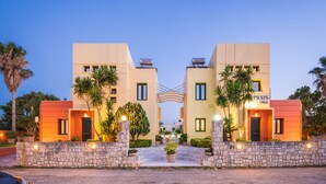 A modern hotel with a symmetrical facade, stone walls, and palm trees. - Daphnis Villas (Platanias)