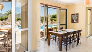 A dining area with a table and chairs, a glass door leading to a pool, and a potted plant on the wall. - Daphnis Villas (Platanias)