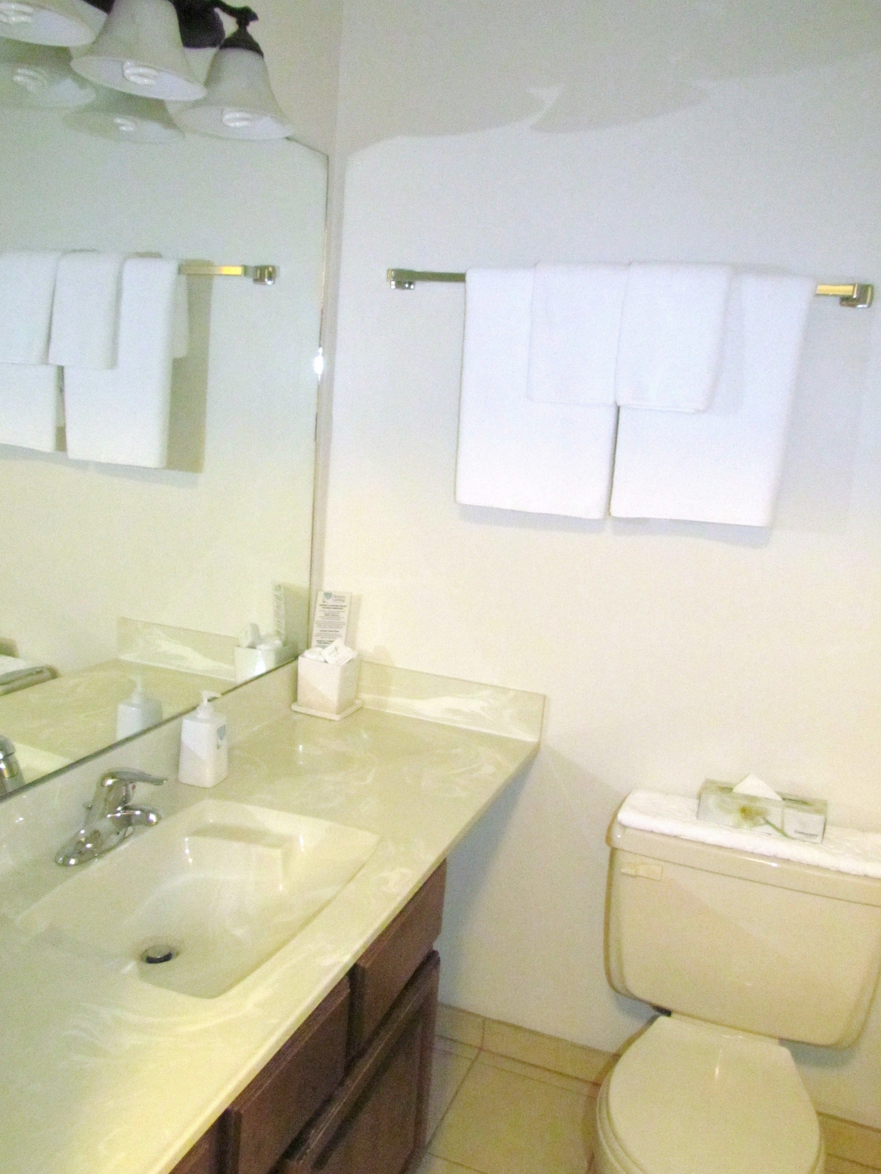Een badkamer met een wastafel, spiegel en toilet. Handdoeken hangen aan een rek.