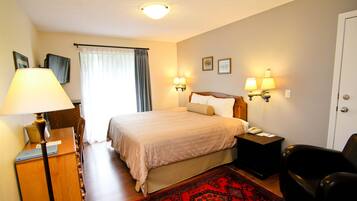 Una habitación de hotel con cama, lámparas de noche, un escritorio con lámpara, una silla, una alfombra roja y una puerta.