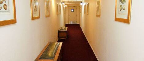 A hallway with framed botanical prints on the walls, a wooden bench, and a red carpet.