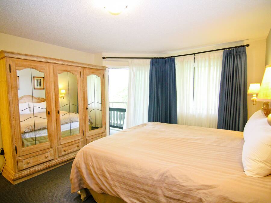 A bedroom with a large bed, a wooden wardrobe, and a balcony with curtains.