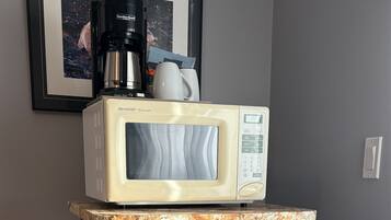 A kitchenette with a microwave, a small refrigerator, and a coffee maker on a wooden shelf.