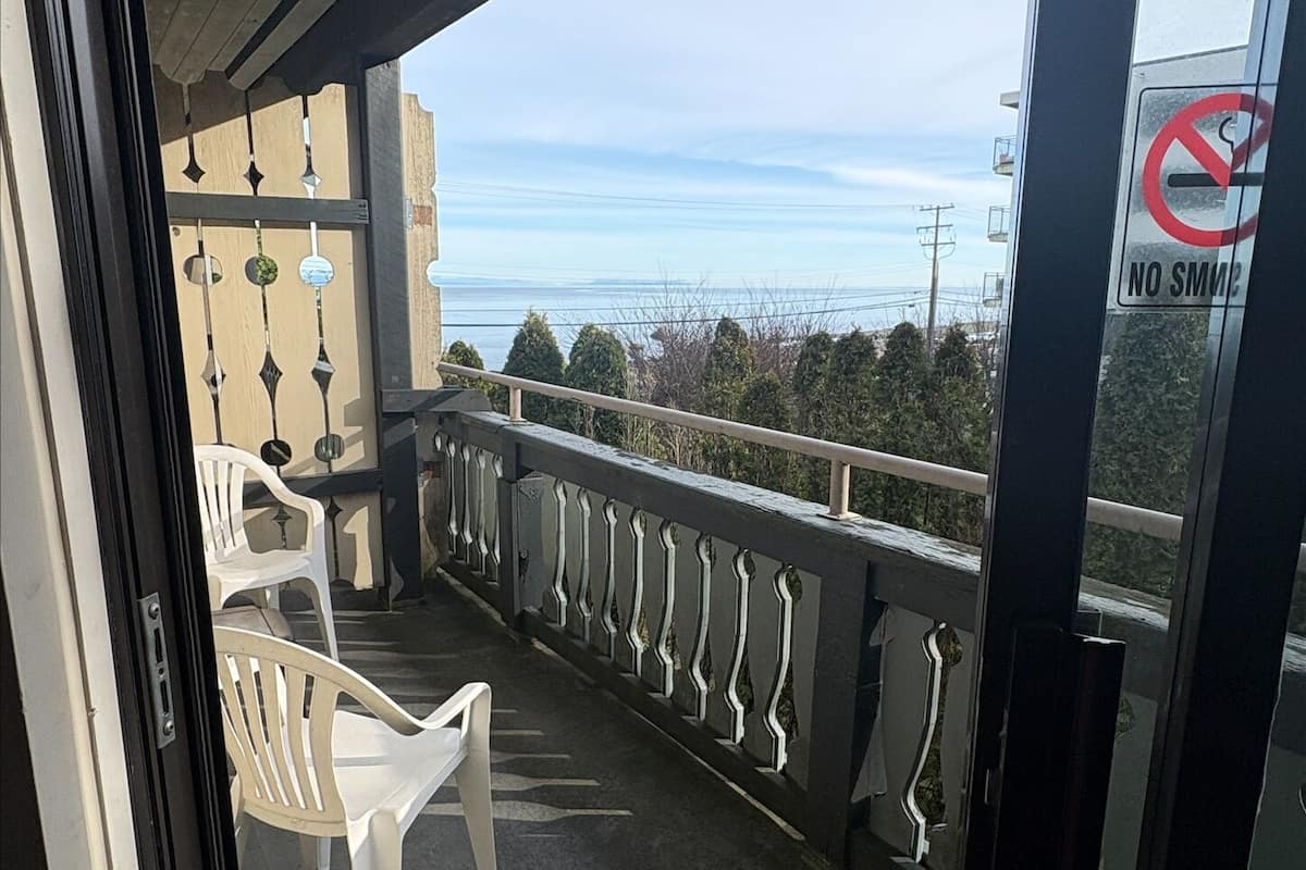 Un balcón con vista al mar, una barandilla y dos sillas blancas de plástico.